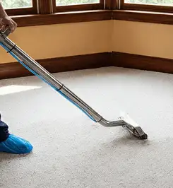Steam carpet cleaning technician using a hot-water extraction wand on a residential carpet, wearing blue protective shoe covers Lakeland, FL.
